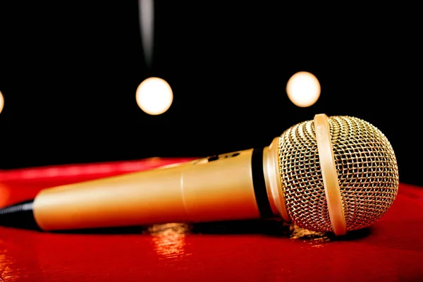 gold microphone on red wooden and dark background with many lights