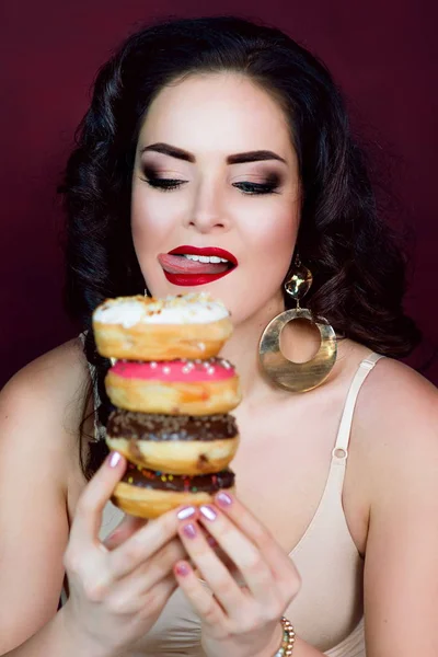 Junge, schöne, attraktive, dunkelhaarige Frau mit bunten, schmackhaften, glasierten Donuts auf Marsala-Hintergrund — Stockfoto