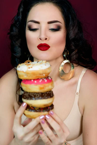 Jovem, bonita, atraente, mulher de cabelos escuros com colorido, saboroso, donuts envidraçados no fundo marsala — Fotografia de Stock