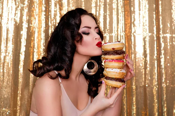 Jonge, mooie, aantrekkelijke, darkh uitgezonden vrouw met kleurrijke, smakelijke, geglazuurde donuts op gouden achtergrond — Stockfoto