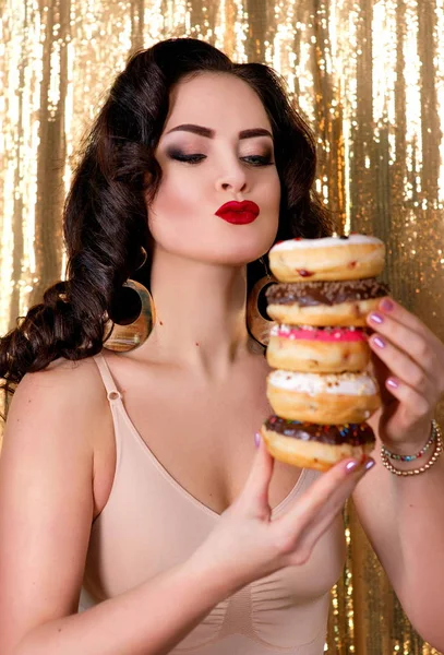 Joven, hermosa, atractiva, mujer de aire oscuro con colorido, sabroso, rosquillas esmaltadas sobre fondo de oro — Foto de Stock