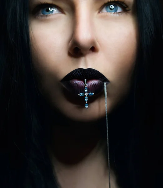 Ritratto di donna dai capelli scuri con labbra scure con croce in bocca — Foto Stock
