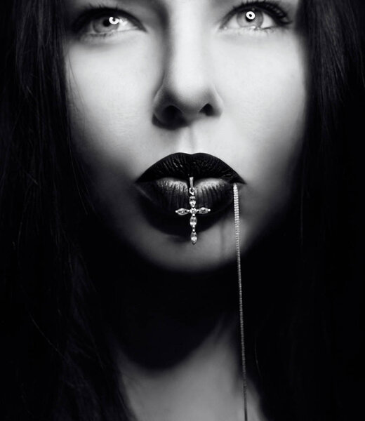 Portrait of dark hair woman with dark lips with cross in her mouth