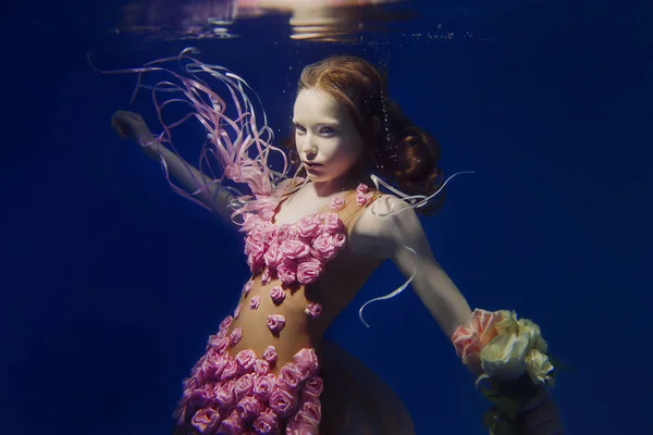 Porträtt av unga vackra röda hår flicka i rosa klänning och med rosor under vattnet — Stockfoto