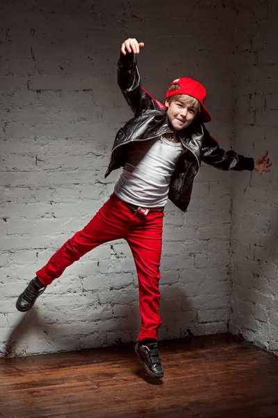 Портрет крутого молодого хлопчика хіп-хопу в червоній шапці і червоних штанях і білій сорочці і чорній шкіряній куртці на горищі — стокове фото