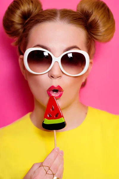 Porträt einer hübschen jungen blonden Frau mit Sonnenbrille und buntem Wassermelonen-Lutscher auf rosa Hintergrund — Stockfoto