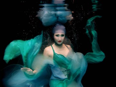 Yüzme havuzunda sualtı siyah zemin üzerine yeşil giysili genç güzel kız portresi