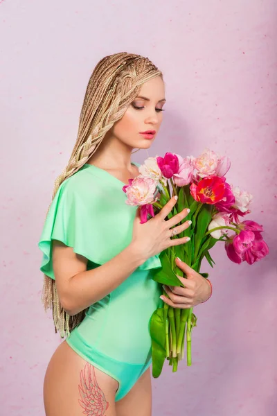 Retrato de hermosa joven atractiva mujer elegante con trenzas africanas con tulipanes en la mano sobre fondo rosa —  Fotos de Stock