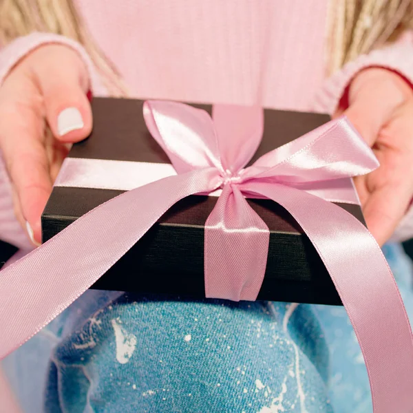 Mani di donna con manicure rosa contenente scatola regalo nera con nastro rosa — Foto Stock