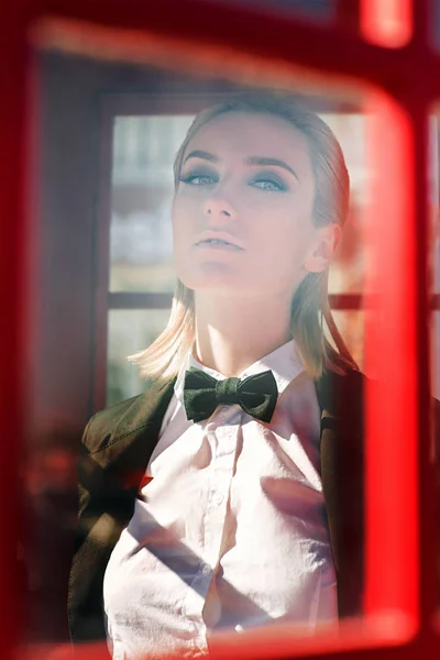 Retrato de mulher loira bonita elegante no homem terno preto na caixa de telefone vermelha — Fotografia de Stock