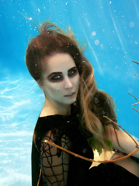 Underwater fashion portrait of beautiful blonde young woman in black dress with grape leaves