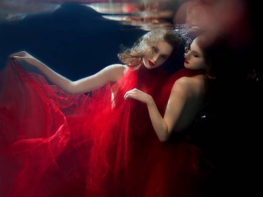 Underwater portrait ot two young beautiful girls with make up in red stylish dresses underwater clipart