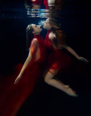 Underwater portrait ot two young beautiful girls with make up in red stylish dresses underwater clipart