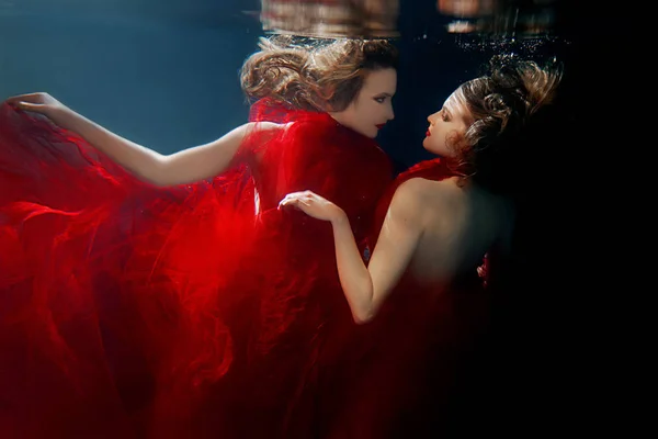 Undervatten porträtt ot två unga vackra flickor med göra upp i röda eleganta klänningar under vattnet — Stockfoto