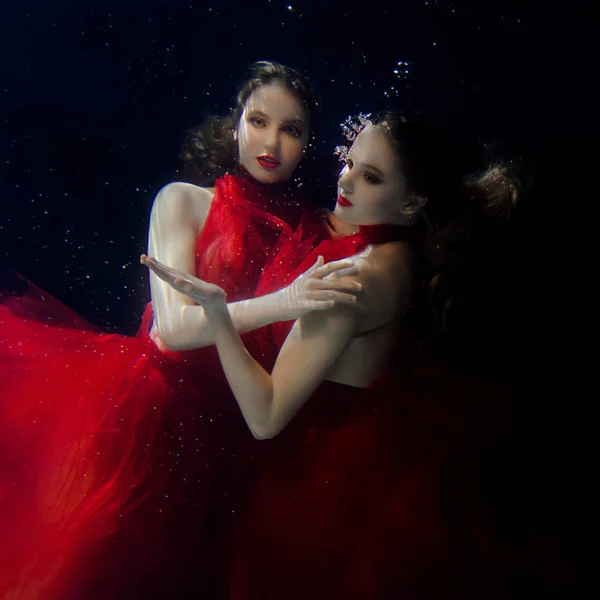 Onderwater portret ot twee jonge mooie meisjes met make-up in rode stijlvolle jurken onderwater — Stockfoto