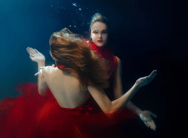 Underwater portrait ot two young beautiful girls with make up in red stylish dresses underwater — Stock Photo, Image