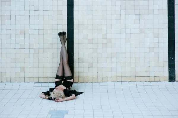 Bella giovane donna bionda sensuale in biancheria intima nera e calze da solo nella piscina vuota — Foto Stock