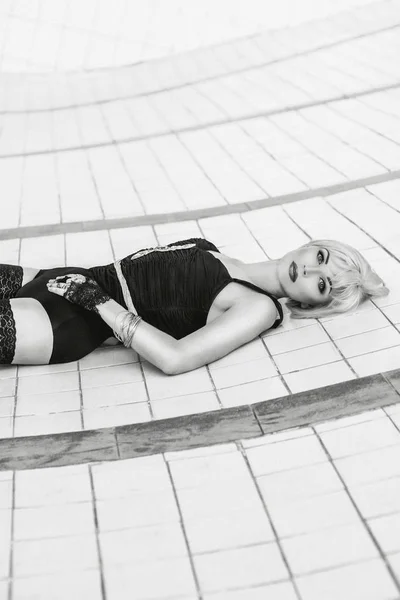 Retrato monocromático de bela jovem loira sensual em roupa interior preta e meias sozinho na piscina vazia — Fotografia de Stock
