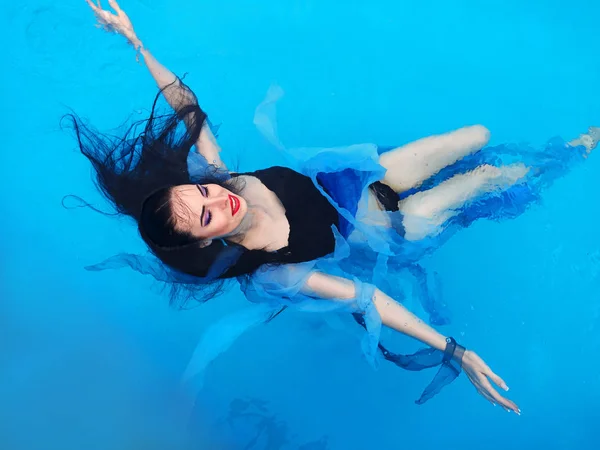 Hermosa mujer de pelo Darl en vestido acostado en el agua en la piscina — Foto de Stock