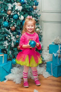 Oturma ve neredeyse gülümseyen sarışın küçük kız süslenen Noel ağacı 