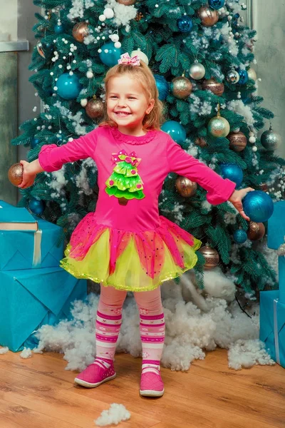 Blond liten flicka sitter och ler nästan dekorerad julgran — Stockfoto
