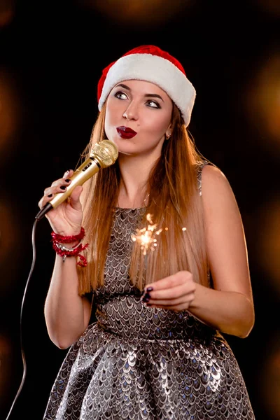 Joven rubia atractiva mujer en rojo sombrero de año nuevo con micrófono y bengala en el canto del escenario —  Fotos de Stock