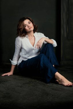 Genç, güzel, üzgün bir aktrisin portresi. Kısa kahverengi saçlı, beyaz gömlekli ve mavi pantolonlu.