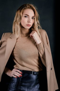 Bej ceketi ve deri gömlek koyu arka plan üzerinde genç çekici güzel sarışın kadın portresi