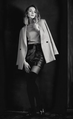 Siyah ve beyaz ceket, deri kıyafet, gaiters, koyu arka plan üzerinde patent ayakkabılar genç çekici güzel sarışın kadın portresi