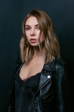 Siyah ceketli, ipek elbiseli, şık, sarışın bir kadının portresi.