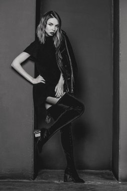 Siyah beyaz portre kısa içinde genç çekici şık sarışın kadın botları giymektedir ve karanlık ile minimalist Oda siyah ceket photo studio duvarlar