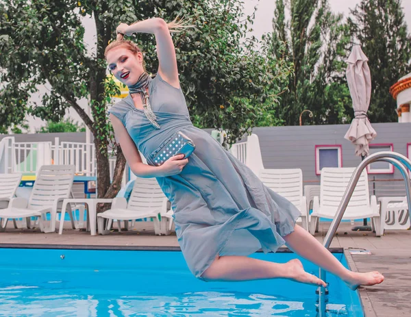 美丽的时尚金发女士在灰色长的礼服下降在游泳池 — 图库照片