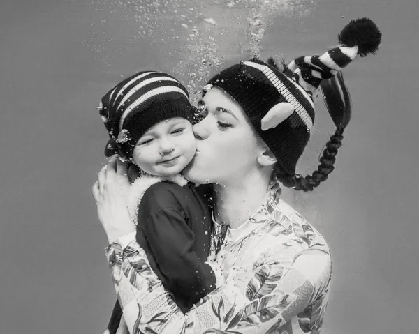 在新的一年里 白人妇女 在水下亲吻她的孩子 圣诞节小精灵在游泳池里穿衣 — 图库照片