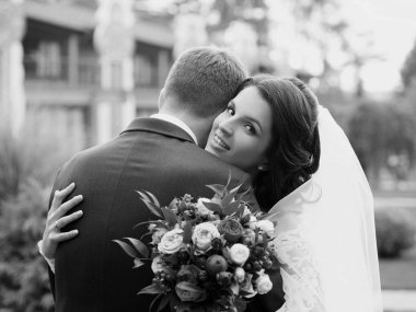 Gülümseyen, mutlu, neşeli gelin damat tutuyor. Düğün çifti (kadın ve erkek) gelinlik ve takım elbiseli. Aşk, aile, şefkat konsepti