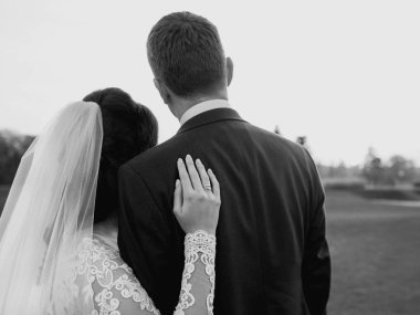 Gelinlik ve takım elbiseli bir çift sahada gün batımını seyrediyor.