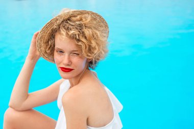 Güzel, gülümseyen kızıl saçlı kadın portresi yüzme havuzunda ya da yaz günü deniz kenarında oturuyor. Yaz, rahatla, sağlık, seyahat, dinlenme konsepti