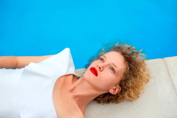beautiful redhead (ginger) curly woman in white swimming suit laying by the swimming pool in summer day. Summer, happiness, relax, wellness, recreation concept