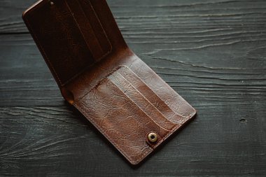 Deri el yapımı, siyah ahşap arka planda kahverengi, boş bir cüzdan. Finans, yoksulluk, para kavramı