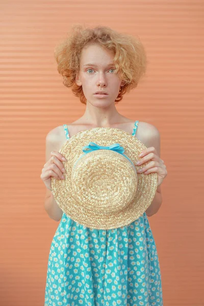 年轻快乐的卷曲红头发的女人穿着蓝色的太阳衣 手里拿着米色背景的草帽 青春的概念 — 图库照片
