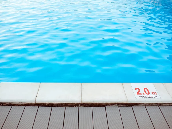 The edge of the swimming pool with the table with information of the depth in English language. Sport, safety, recreation and relax concept.