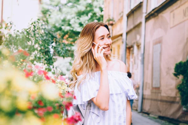 beautiful young blonde woman walking on the street and talking on a cell phone,the girl laughs and smiles,the perfect photo for mobile advertising  travel,shopping for magazines,photo -style lifestyle