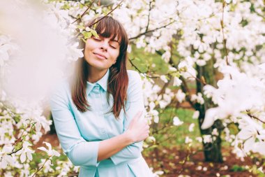  tatlı, güzel kız üzerinde yumuşak arka plan Manolya çiçek çiçekler, saçları, esen rüzgar ayakta güneş ışınları yumruk, beyaz pembe elbisenin içinde kapalı gözlerini ve ihale gülümseyen küçük bir gülümseme ile standları