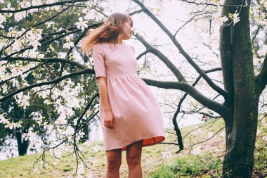 tatlı, güzel kız üzerinde yumuşak arka plan Manolya çiçek çiçekler, saçları, esen rüzgar ayakta güneş ışınları yumruk, beyaz pembe elbisenin içinde kapalı gözlerini ve ihale gülümseyen küçük bir gülümseme ile standları