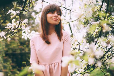 tatlı, güzel kız üzerinde yumuşak arka plan Manolya çiçek çiçekler, saçları, esen rüzgar ayakta güneş ışınları yumruk, beyaz pembe elbisenin içinde kapalı gözlerini ve ihale gülümseyen küçük bir gülümseme ile standları