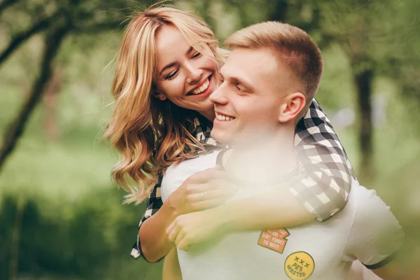 Foto de família gentil de belo casal jovem.Eles ficam no fundo do jardim da maçã.A mulher abraçando o homem por trás e olhando para ele e sorrindo. — Fotografia de Stock