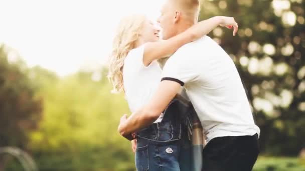 Photo of a young couple. A man in a white T-shirt turns a girl in a White T-shirt and denim overalls against the backdrop of an apple garden. Cute gentle photo ideal for advertising or banner, soft focus — Stock Video