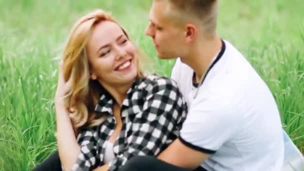 Familienfoto. Mann und Frau liegen auf einer karierten Matte im Apfelgarten. Sie schauen einander an, lächeln und küssen sich. auf dem Foto herrscht eine Atmosphäre der Liebe, Ruhe und des Glücks — Stockvideo
