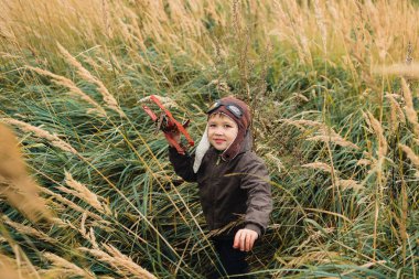 Bir çocuk kırmızı bir uçak ile oynuyor. Çocuk uzun otların bir alana
