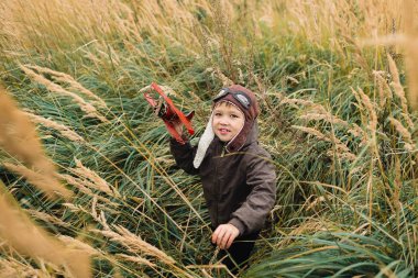 Bir çocuk kırmızı bir uçak ile oynuyor. Çocuk uzun otların bir alana