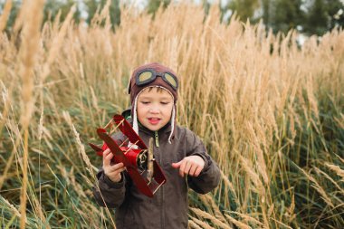 Bir çocuk kırmızı bir uçak ile oynuyor. Çocuk uzun otların bir alana